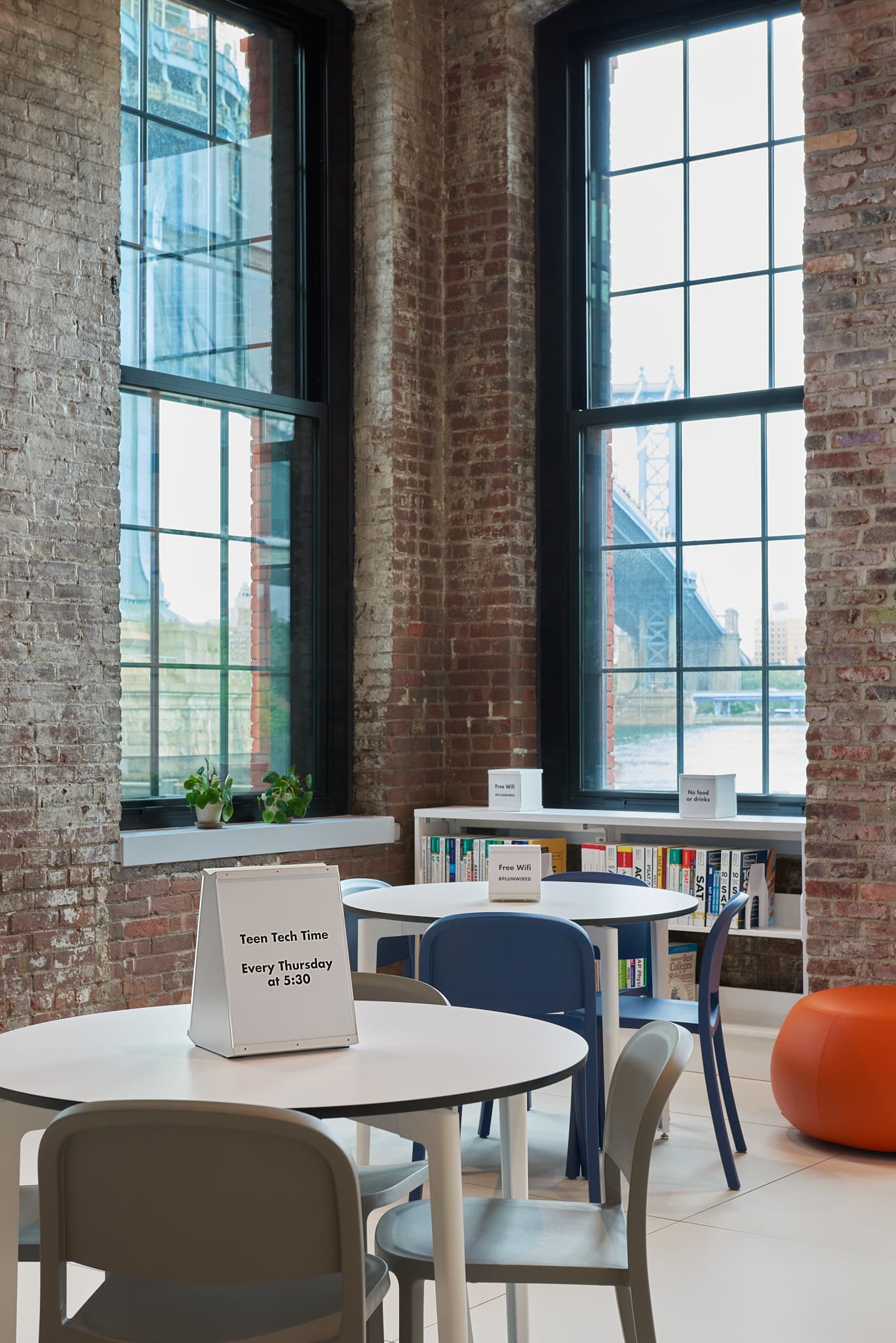 Photo of work tables, with changeable message signs on the tables advertising upcoming events and free wifi. In the background are cubes on the book shelves labeling each section.