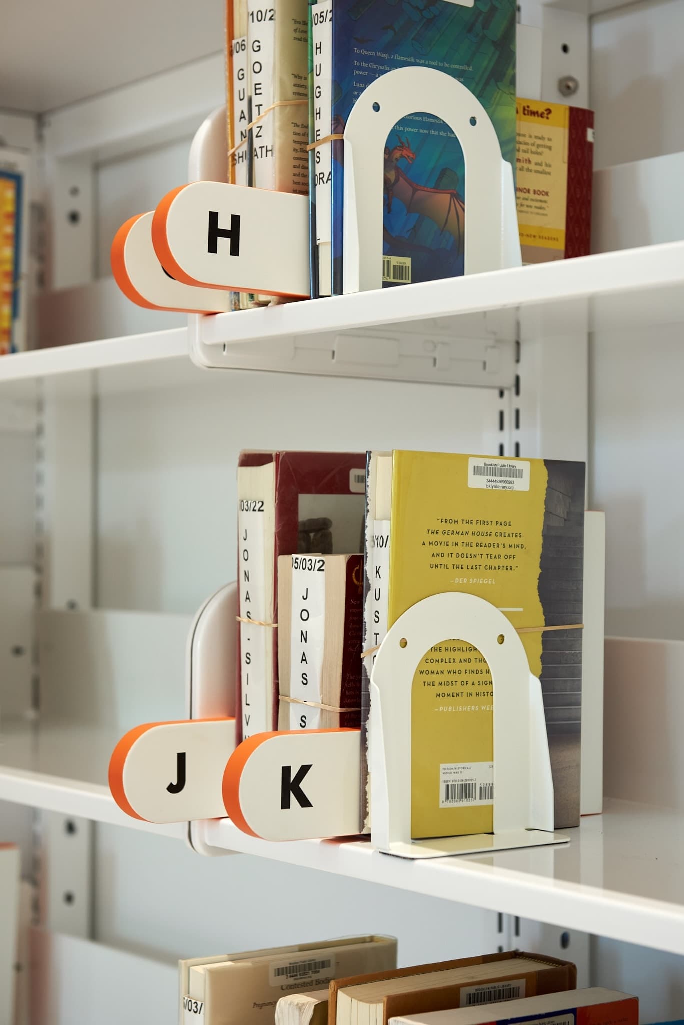 Photo of book dividers on the hold shelves, with alphabet letters, shaped and colored similarly to the inverse of the kids area wall cutout